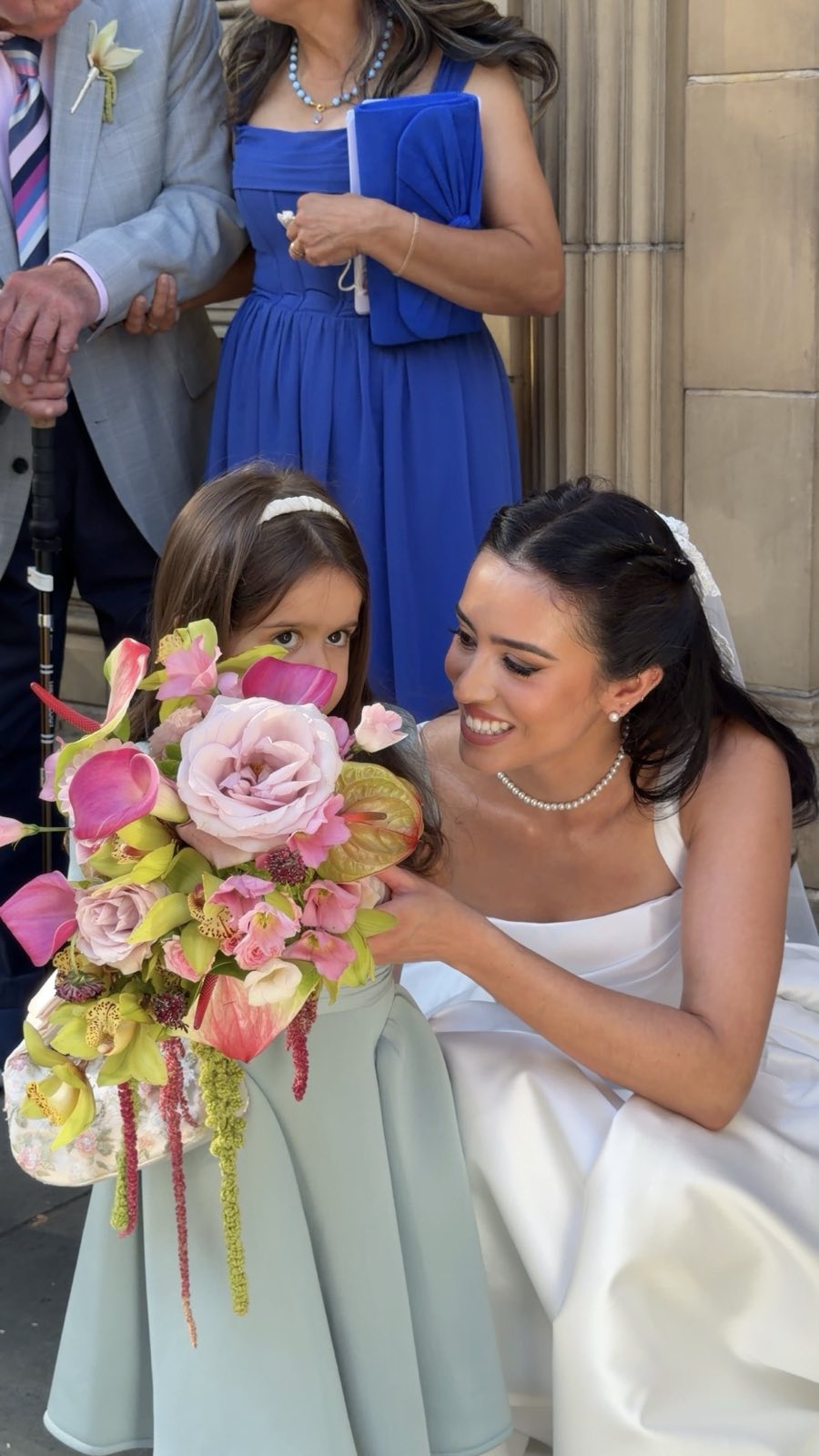 Bride kneeling beside a little flower girl holding a pink bouquet