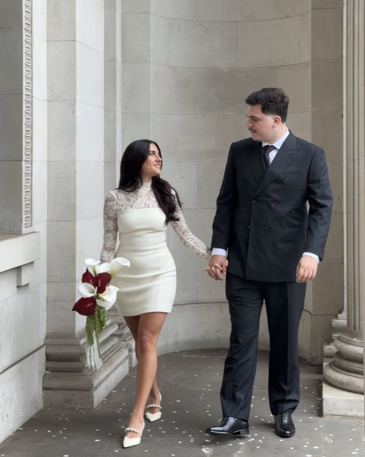 Bride and groom walking hand in hand past stone columns in London