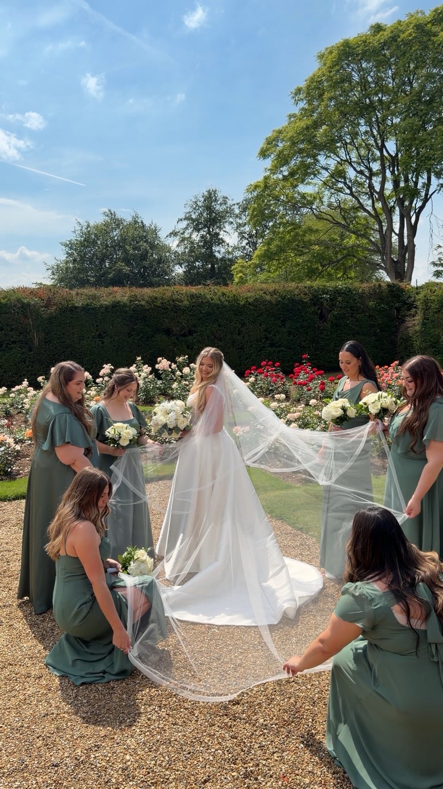 Bride with her bridesmaids holding her long veil in a garden