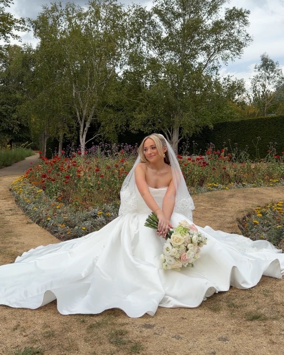 Bride sitting in a flower garden in her satin wedding dress